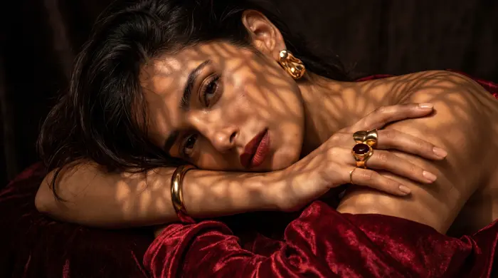 Mulher repousando sob luz filtrada, usando anéis e pulseira de ouro